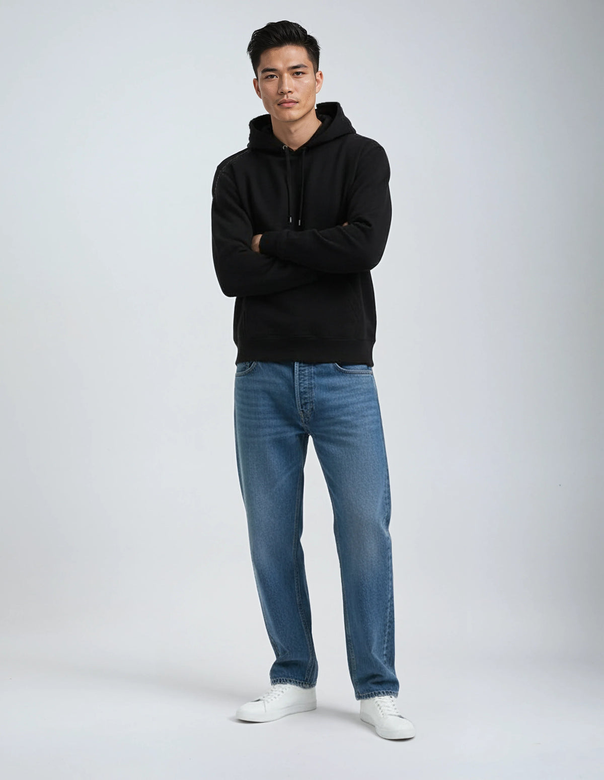 Man wearing a black hoodie, blue jeans, and white shoes on a white background